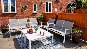 Un patio con muebles blancos, una mesa con bebidas y plantas en macetas.