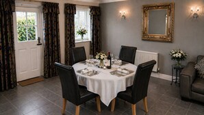 Comedor con mesa redonda para cuatro, sillas de cuero negro, mantel blanco y un florero con flores.