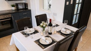 Uma sala de jantar com uma mesa posta para quatro pessoas, incluindo pratos, talheres, copos e uma garrafa de vinho.