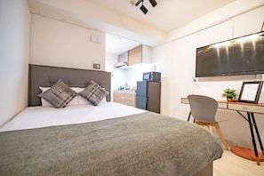 A modern hotel room with a large bed, a desk with a chair, a flat-screen TV, and a kitchenette in the background. - Grandouce Shinkitano (Osaka)