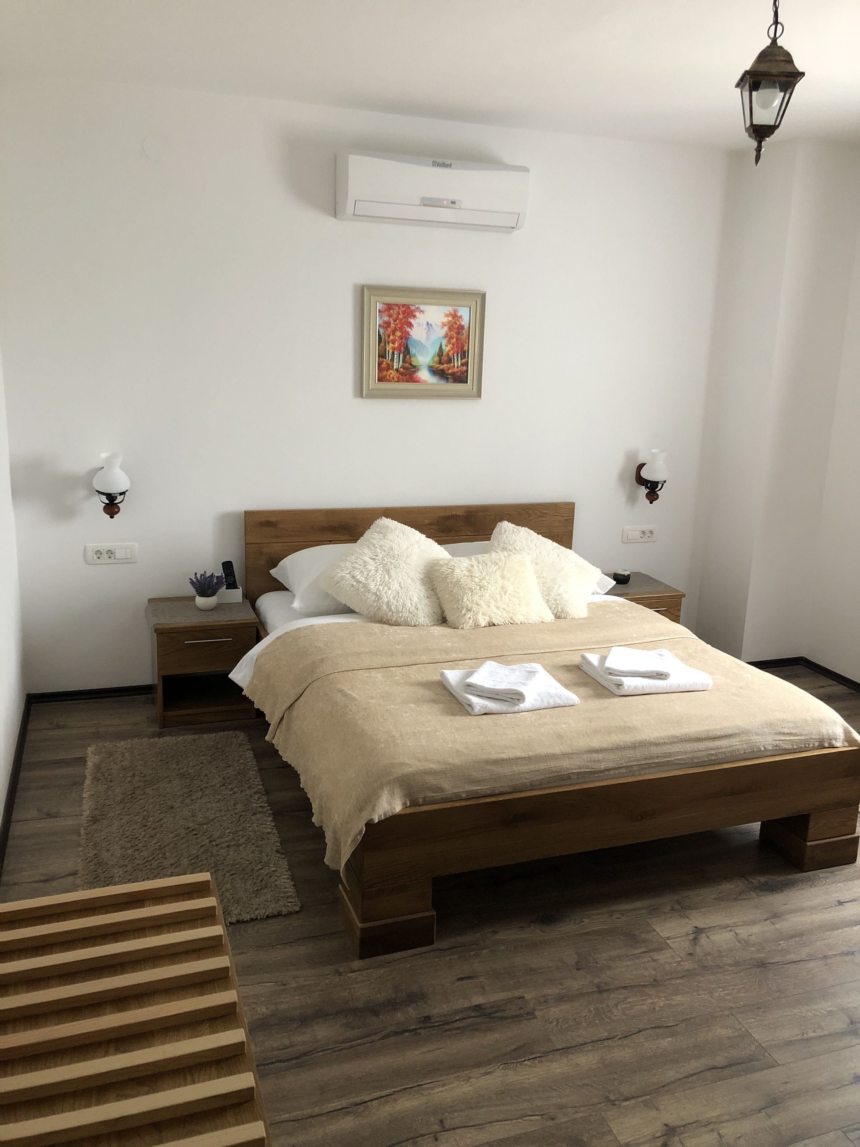 A bedroom with a wooden bed, white bedding, a painting on the wall, and a ceiling fan.