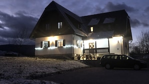 Ein großes Haus mit geneigtem Dach, ein Auto davor und verschneiter Boden.
