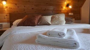 Ein ordentlich bezogenes Bett mit weißen Leinen und zusammengerollten Handtüchern, ein Holz-Kopfbrett und zwei Nachttischlampen.