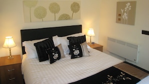 A neatly made bed with a black headboard, two bedside lamps, and decorative pillows. - Macbeth Cottage (Stratford-upon-Avon)