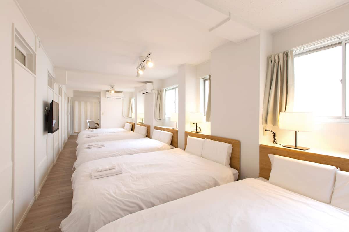 A hotel room with three beds, a TV, and a window with curtains.