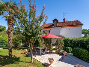 Una casa con techo de tejas, un patio con mobiliario exterior y un jardín con diversas plantas.