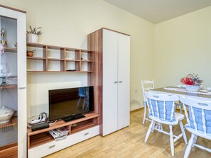 Una sala de estar moderna con un televisor de pantalla plana, estanterías de madera, un armario blanco y un comedor con mesa y sillas.