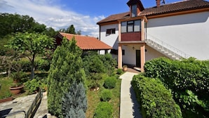 A two-story house with a red-tiled roof, a small balcony, and a garden with various plants and trees. - Apartment Franjo by Interhome (Opatija/Ika)