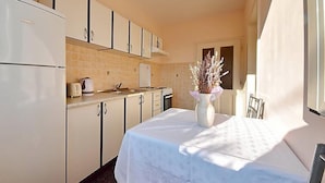 A compact kitchen with white cabinets, a dining table with a white tablecloth, and a vase with dried flowers. - Apartment Franjo by Interhome (Opatija/Ika)