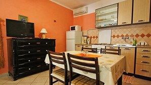 A compact kitchen with a dining area, featuring a TV, a refrigerator, a stove, and wooden cabinets. - Apartment Dijana by Interhome (Korcula/Prigradica)