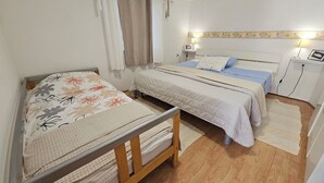 A bedroom with two beds, a wooden floor, a window with curtains, and a wall-mounted lamp. - Apartment Dijana by Interhome (Korcula/Prigradica)
