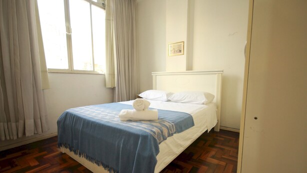 A bedroom with a bed, white curtains, a window, and a wooden floor. - Gohouse - Baependi 503 (Rio de Janeiro)