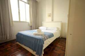 Une chambre à coucher avec un lit, des rideaux blancs, une fenêtre et un plancher en bois.