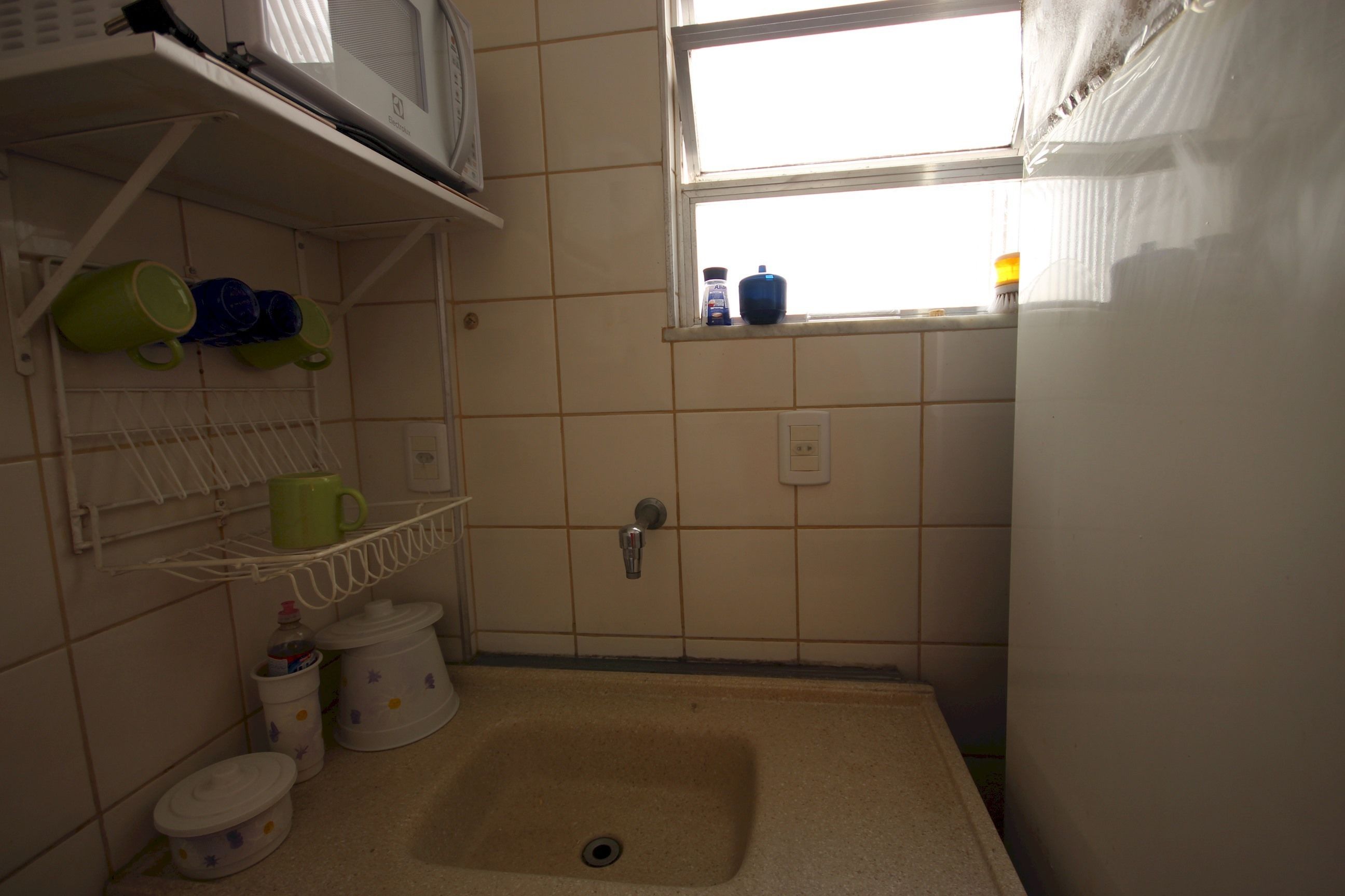 A small bathroom with a sink, a window, and shelves with mugs and containers.