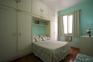 Un dormitorio con cama, armario y ventana con cortinas.