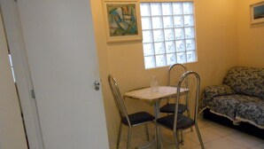 Une petite pièce comprenant une table à manger, des chaises, un canapé, une fenêtre avec des stores et un tableau accroché au mur.