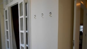 Un couloir avec une porte blanche, une porte entrouverte et trois crochets fixés au mur.