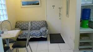 Une petite pièce, de taille modeste, comprenant un canapé, un fauteuil, une petite table, une porte, un tableau accroché au mur et un distributeur d’eau.