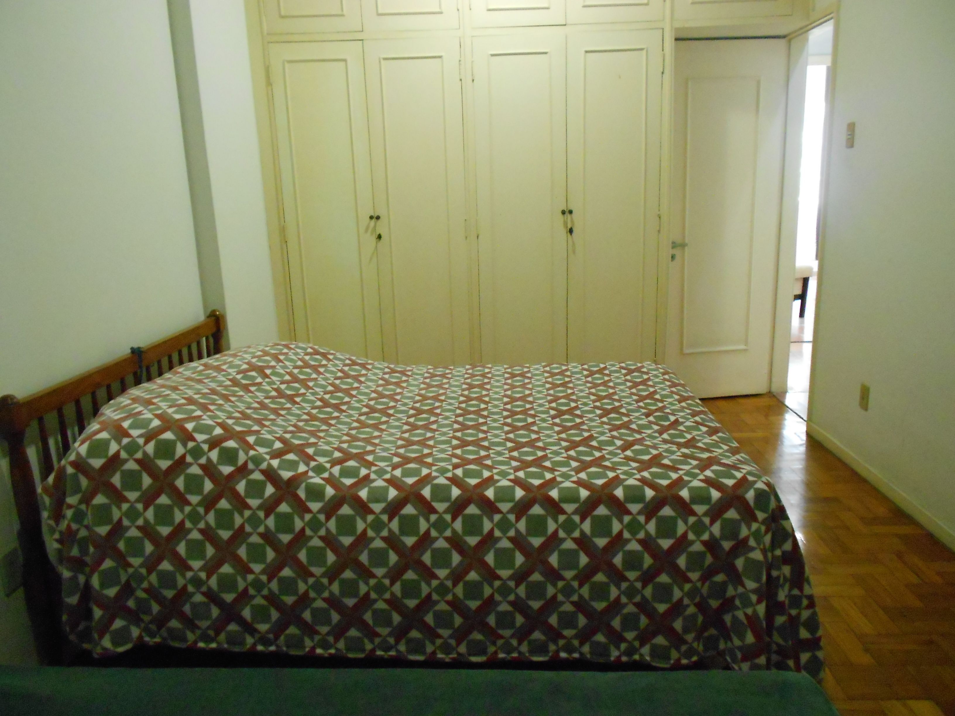 Ein Schlafzimmer mit einem Bett, einem Holzschrank und einer Tür zu einem weiteren Raum.
