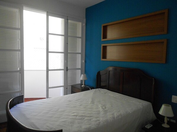 A bedroom with a bed, a chair, a nightstand, and a lamp. - Gohouse - Atlantica 702 B (Rio de Janeiro)