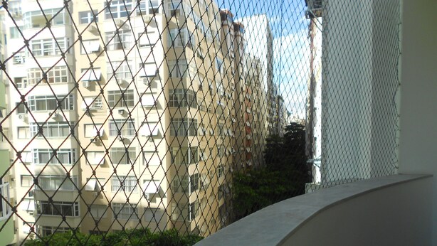 A chain-link fence with a building in the background. - Gohouse - Atlantica 702 B (Rio de Janeiro)