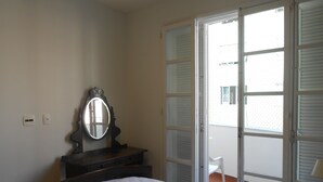 A bedroom with a bed, a dresser, a mirror, and a sliding glass door leading to an outdoor area. - Gohouse - Atlantica 702 B (Rio de Janeiro)