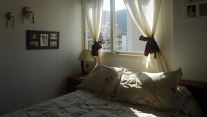 A bedroom with a bed, a nightstand, a lamp, and a window with curtains. - Gohouse - Anibal 604 (Rio de Janeiro)