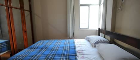 A bedroom with a bed, a window with curtains, and a wooden wardrobe.