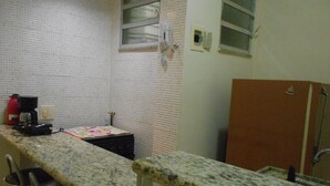 Una cocina con encimera de granito, un lavamanos pequeño, un hervidor rojo y una ventana con persianas.