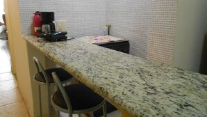 Una cocina con encimera de granito, dos taburetes de bar, una cafetera y un lavamanos pequeño.