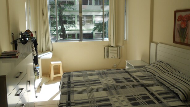 Un dormitorio con cama, ventana con cortinas, ventilador de techo y radiador.