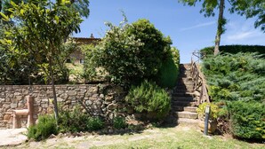 Un escalier en pierre menant à un bâtiment, entouré d’une végétation luxuriante et d’un mur de pierre.