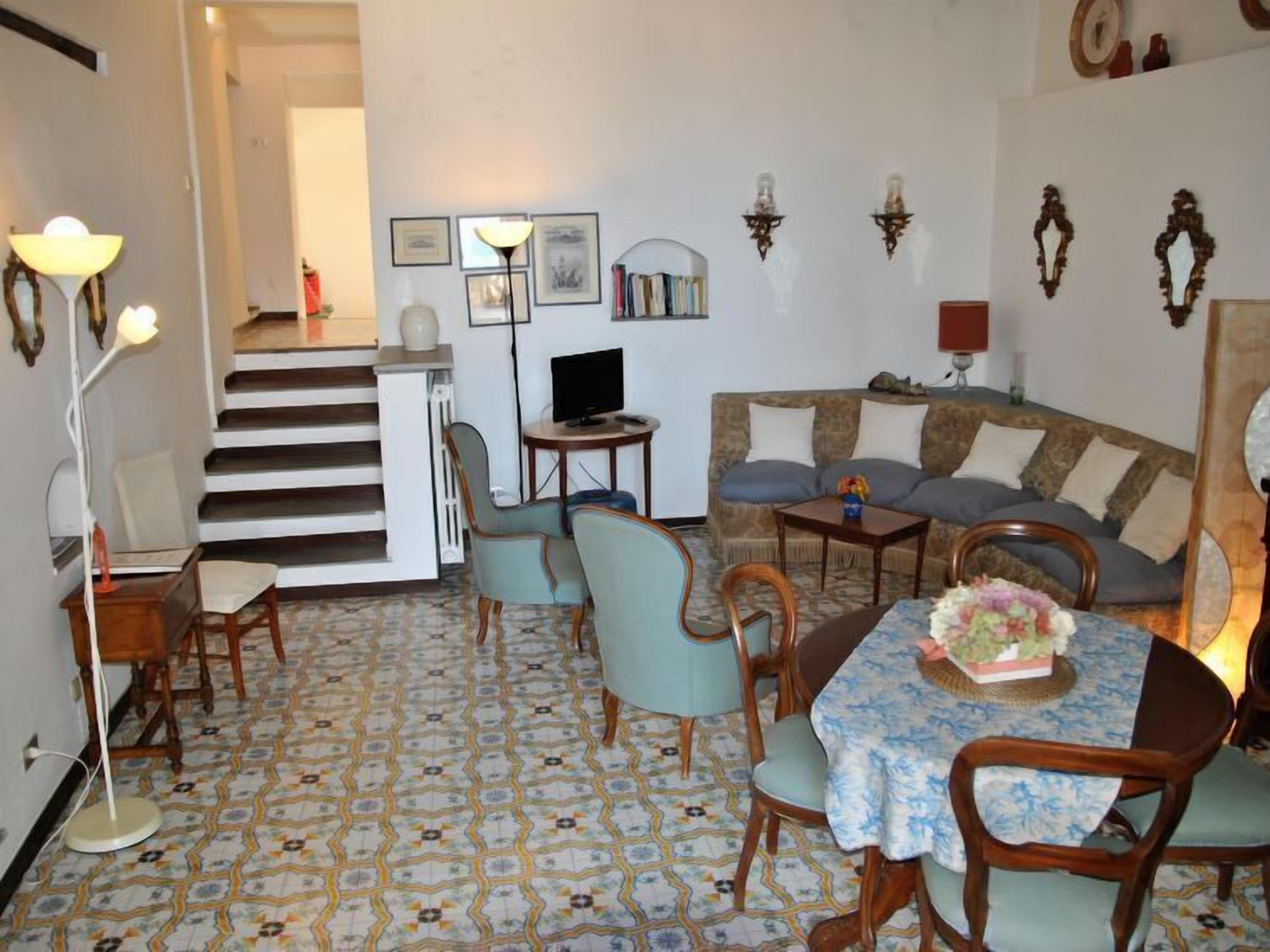 Ein Wohnzimmer mit einer Couch, Sesseln, einem Esstisch und einer Treppe, die in einen anderen Raum führt.