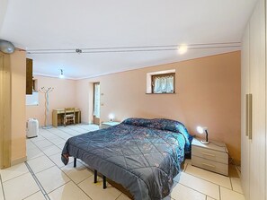 Et soveværelse med seng, natbord, lampe og et lille vindue med gardiner.