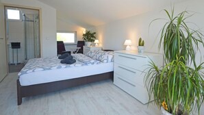 Een moderne slaapkamer met een bed, nachtkastje, lamp en potplanten.