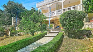 Un edificio de dos pisos con un balcón, paredes de piedra y un camino de piedra que conduce a la entrada.