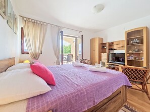 Une chambre à coucher avec un lit, une télévision, une armoire en bois et un balcon.