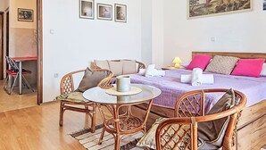 Una habitación con una cama, una mesa de comedor, sillas de mimbre, una mesita redonda y un cuadro en la pared.