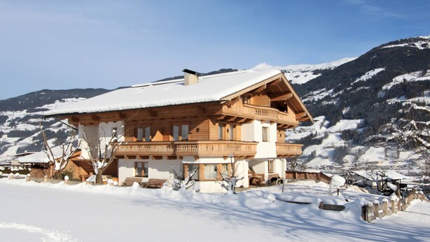Un chalet in legno con un balcone, circondato da montagne innevate.