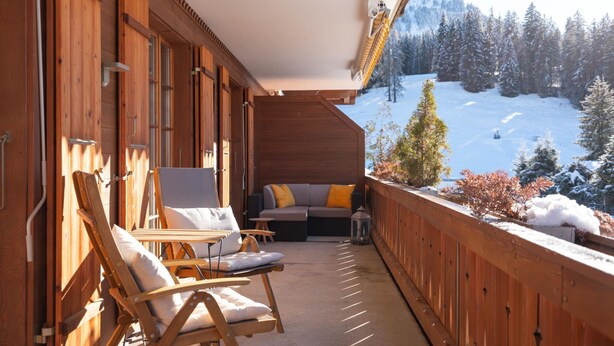 A wooden balcony with two lounge chairs and a sofa, overlooking a snowy mountain landscape. - Fichte (Marija) by Interhome (Saanenmöser)