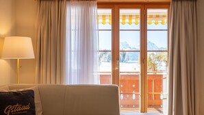 A room with a sofa, a lamp, and a view of a snowy mountain landscape through a sliding glass door. - Fichte (Marija) by Interhome (Saanenmöser)