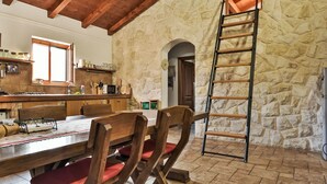 A rustic kitchen with stone walls, wooden beams, a dining area with red cushioned chairs, and a ladder against the wall. - Malu Sun II by Interhome (Brodarica)