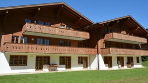 A multi-story wooden chalet with balconies, large windows, and a well-maintained lawn. - Jacqueline 12 by Interhome (Gstaad)