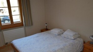 A bedroom with a bed, a nightstand, a window, and a radiator. - Jacqueline 12 by Interhome (Gstaad)