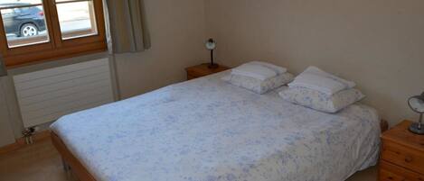 A bedroom with a bed, a nightstand, a window, and a radiator.
