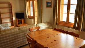 A cozy living room with a wooden dining table, a sofa, and a TV. - Jacqueline 12 by Interhome (Gstaad)