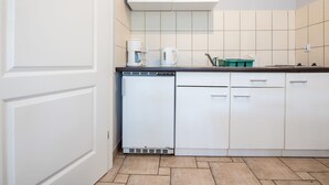 Kompakti keittiö, jossa on valkoiset kaapit, astianpesukone ja kahvinkeitin.