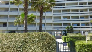 Un hôtel à plusieurs étages doté de balcons, de palmiers et d’une haie bien entretenue à l’avant.