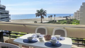 Un balcon avec une table dressée pour deux personnes, offrant une vue sur une plage et l’océan.