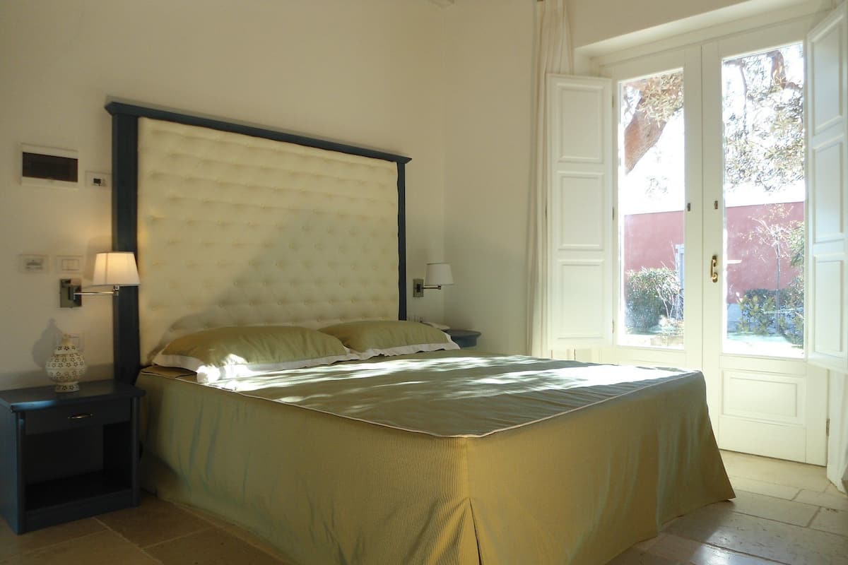 A bedroom with a bed, bedside lamps, a nightstand, and a door leading to a balcony.